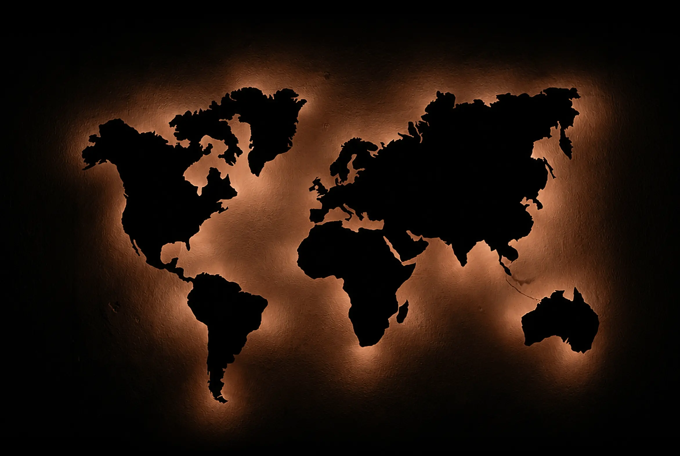 Backlit world map silhouette glowing warm amber against a dark wall