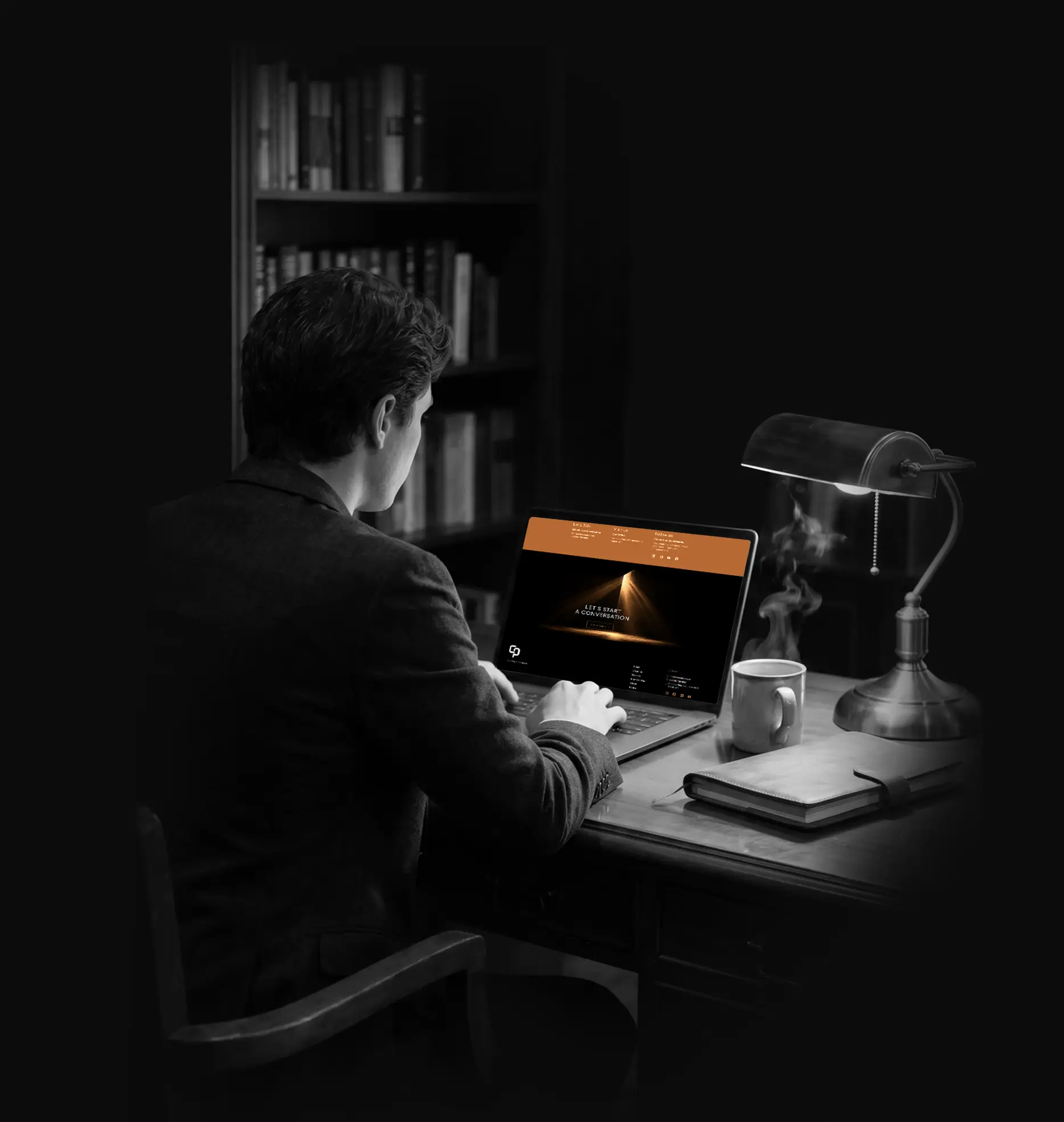 Man at a desk typing on a laptop showing the Concept Plus contact page, lit by a banker's desk lamp
